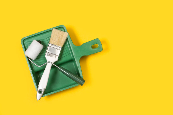 Um rolo de pintura e um pincel em uma bandeja de pintura em um fundo amarelo - Foto, Imagem