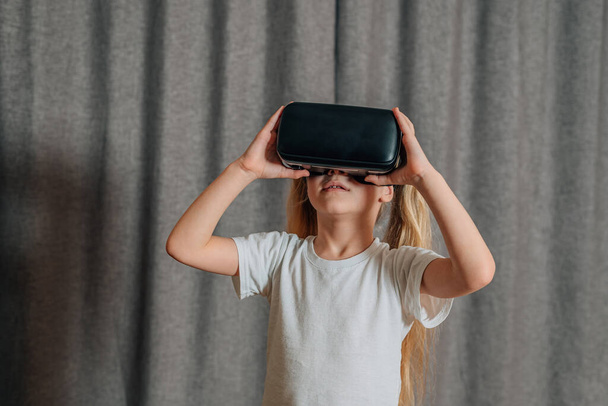 κορίτσι παιδί στο σπίτι σε εικονική πραγματικότητα γυαλιά VR βλέποντας βίντεο, παίζοντας παιχνίδια. Τα σύγχρονα παιδιά γνωρίζουν καλά τις τεχνολογικές καινοτομίες. γενεά άλφα. Υψηλής ποιότητας φωτογραφία - Φωτογραφία, εικόνα