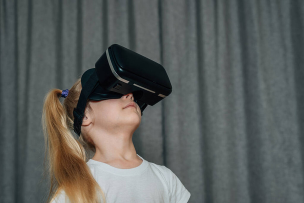 child girl at home in virtual reality VR glasses watching video, playing games. modern children are well versed in technological innovations. generation alpha. High quality photo - 写真・画像