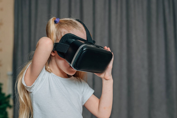 Evde sanal gerçeklik gözlüklü çocuk video izleyip oyun oynuyor. Modern çocuklar teknolojik yenilikler konusunda çok bilgilidirler. Alfa kuşağı. Yüksek kalite fotoğraf - Fotoğraf, Görsel