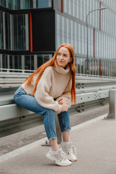 Girl with red hair sitting on the road in city. Portrait of a beautiful girl on the streets of the beautiful city. Mature woman with red hair and freckles looking at camera. - Photo, image