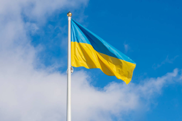 Ukraińska flaga na maszcie flagowym trzepocze na wietrze o błękitne niebo z chmurami. Koncepcja: walka Ukraińców o niepodległość, wojna między Ukrainą a Rosją. - Zdjęcie, obraz