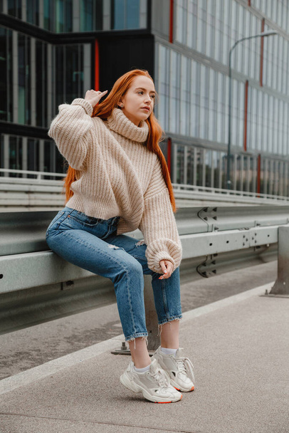 Girl with red hair sitting on the road in city. Portrait of a beautiful girl on the streets of the beautiful city. Mature woman with red hair and freckles looking at camera. - Foto, Imagen