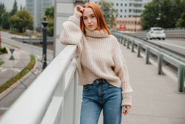 Outdoor portrait of girl standing on stairs near bridge in Warsaw. Portrait of girl on bridge in the street. Attractive european woman in sweater and beret exploring country in vacation. - 写真・画像