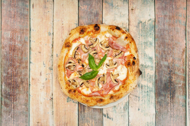 Pizza with slices of cooked ham, mozzarella cheese and mushroom slices with an aromatic basil leaf in the center - Photo, Image