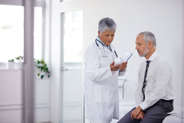 Ça devrait beaucoup aider. Un médecin mature donne une bouteille de pilules à l'un de ses patients lors d'un check-up. - Photo, image