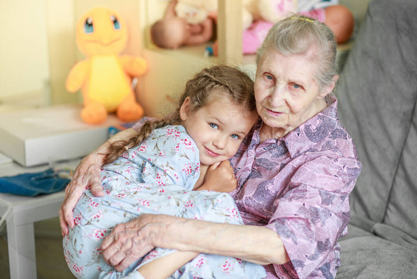 Retrato de una anciana y una niña, abuela abraza a su nieta, lazos familiares, vejez y juventud, 90 años, arrugas en una cara vieja, hermosa vejez, una mujer y un niño. - Foto, imagen