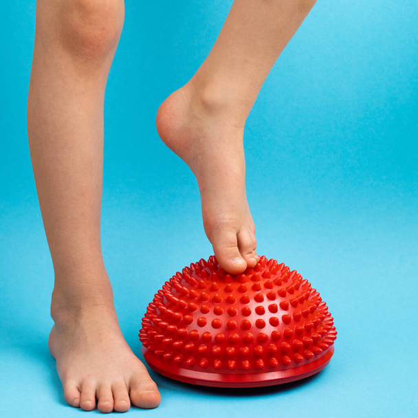 niños pies con un equilibrador rojo sobre un fondo azul claro, tratamiento y prevención de pies planos, deformidad valgus del pie - Foto, Imagen