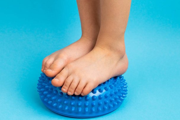 niños pies con un equilibrador azul sobre un fondo azul claro, tratamiento y prevención de pies planos, deformidad valgus del pie - Foto, imagen