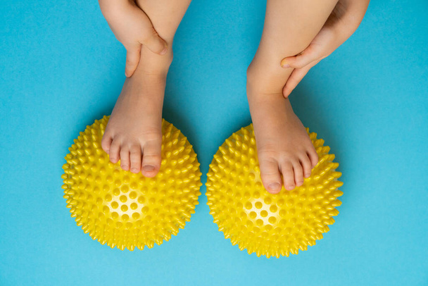niños pies con un equilibrador amarillo sobre un fondo azul claro, tratamiento y prevención de pies planos, deformidad valgus del pie - Foto, Imagen