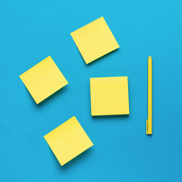 Набор жёлтой бумаги и жёлтая ручка на синем фоне. Стильные канцелярские принадлежности. - Фото, изображение
