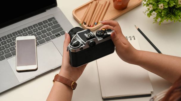 Imagen de cerca, manos femeninas sosteniendo una cámara retro sobre su escritorio de oficina moderno. fotógrafo, blogger, freelancer - Foto, imagen