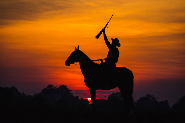 Landschaft Silhouette Cowboy Pferd mit Reiten eine Waffe der Hintergrund ist die Sonne - Foto, Bild