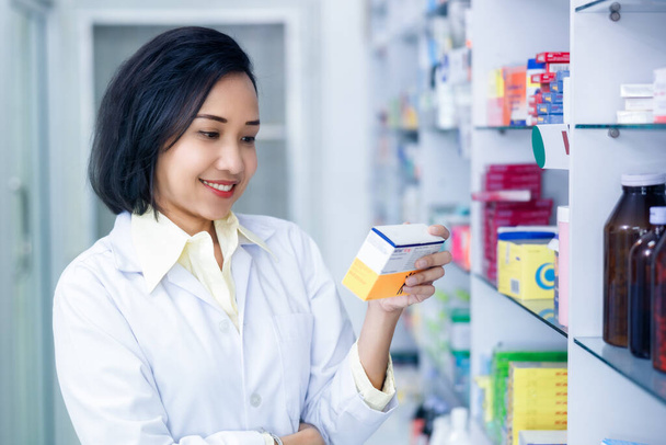 Asain female pharmacist holding and looking medicine packet in drugstore Thailand - Valokuva, kuva