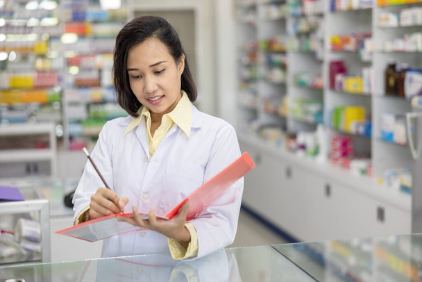 farmacista donna asiatica al lavoro in farmacia e felice di lei durante l'utilizzo degli appunti. Medicina e concetto di assistenza sanitaria - Foto, immagini