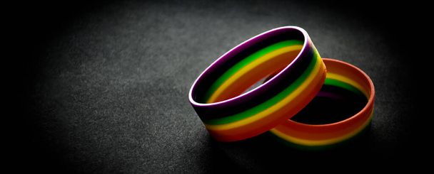 Pulseras de arcoíris de goma sobre fondo negro, luz de neón editada, símbolo lgbt, concepto para celebraciones de comunidades lgbtq + en el mes de orgullo en todo el mundo. - Foto, Imagen