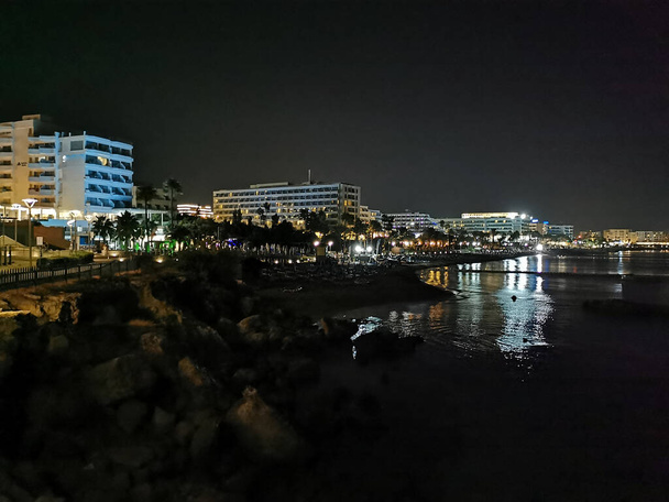 Blick von der Böschung auf Protaras bei Nacht: Strand, Promenade, Meer und Hotels vor schwarzem Himmel. - Foto, Bild