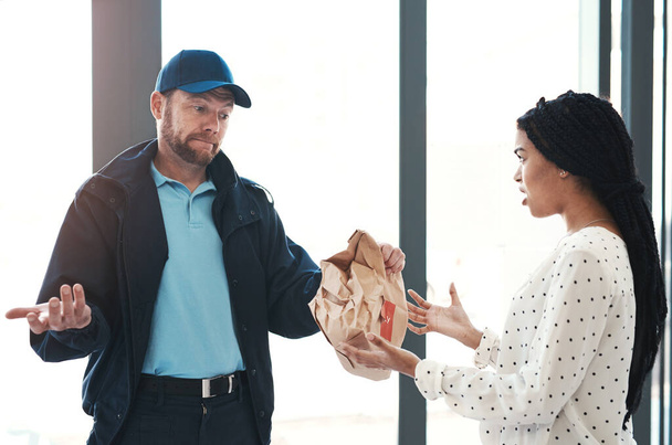 Im sorry but theres nothing I can do about this. Shot of a handsome delivery man negotiating with a dissatisfied female customer in the lobby. - Photo, Image