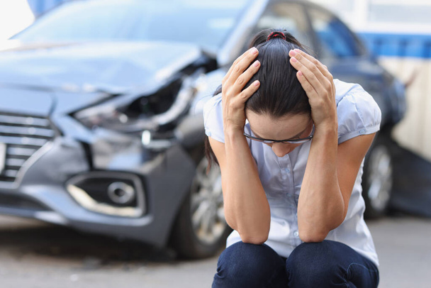 Una mujer joven en un coche roto se sienta sosteniendo la cabeza - Foto, Imagen