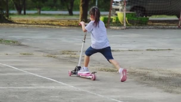 Schattige kleine meisjes rijden scooter op de weg in het park buiten op zomerdag. meisje spelen buiten met scooter. Actieve vrijetijdsbesteding en buitensport voor kinderen - Video