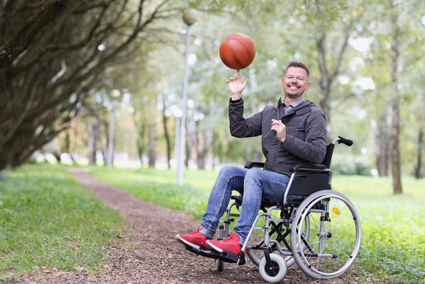 Felice uomo sulla sedia a rotelle gira la palla al dito nel parco - Foto, immagini