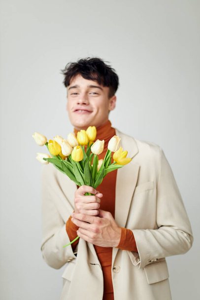 Photo young boyfriend in white jacket with a bouquet of yellow flowers elegant style Lifestyle unaltered - Foto, Imagen