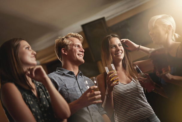 Een drankje en een lach delen. Shot van een groep vrienden die zich vermaken in de bar. - Foto, afbeelding