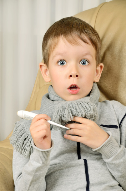 angstige jongen met een thermometer in zijn handen op zoek wide-eyed - Foto, afbeelding