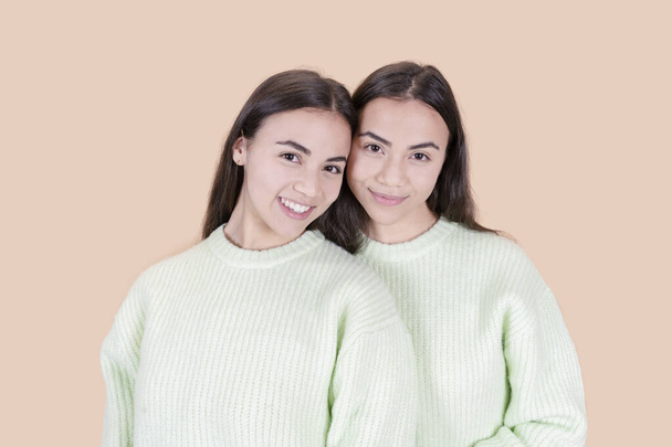 closeup of two pretty twin sisters beige background - Photo, Image