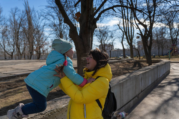 Happy mother and daughter. A little girl jumping into her parent's arms. A woman and her baby face to face. A sunny spring day. Side view. - Foto, imagen