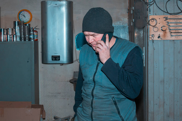 Porträt eines männlichen Arbeitnehmers am Arbeitsplatz in Großaufnahme, der mit dem Handy spricht - Foto, Bild