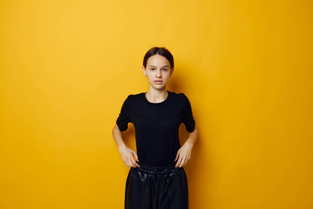 beautiful girl in a black T-shirt and pants smile yellow background - Fotó, kép