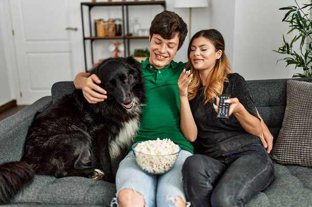 Νεαρό καυκάσιο ζευγάρι βλέποντας ταινία κάθεται στον καναπέ με το σκυλί στο σπίτι. - Φωτογραφία, εικόνα