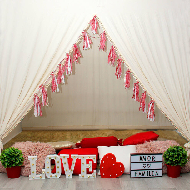 White teepee with red decorations, cushions, a sign that says "Love and family" ready to enjoy and play with the children at a sleepover or a romantic dinner for a couple - Фото, изображение