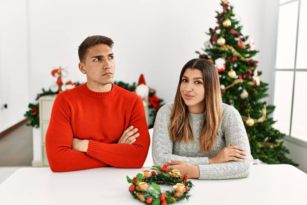 Junges hispanisches Paar sitzt an Weihnachten am Tisch und lächelt zur Seite und starrt nachdenklich weg.  - Foto, Bild