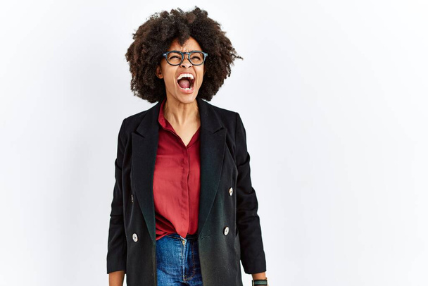 African american woman with afro hair wearing business jacket and glasses angry and mad screaming frustrated and furious, shouting with anger. rage and aggressive concept.  - Foto, afbeelding