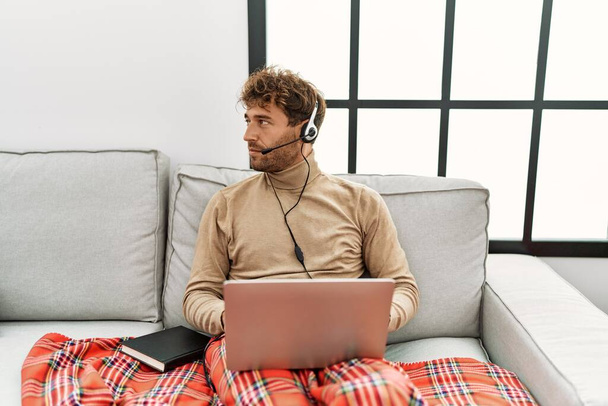 Young handsome man with beard wearing operator headset working from home looking to side, relax profile pose with natural face and confident smile.  - Zdjęcie, obraz