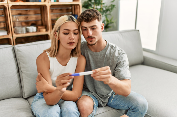 Joven pareja caucásica con expresión seria sosteniendo prueba de embarazo en casa. - Foto, imagen