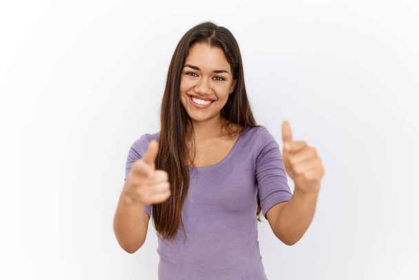 Jonge brunette vrouw staat bij geïsoleerde achtergrond wijzende vingers naar camera met gelukkig en grappig gezicht. goede energie en vibes.  - Foto, afbeelding