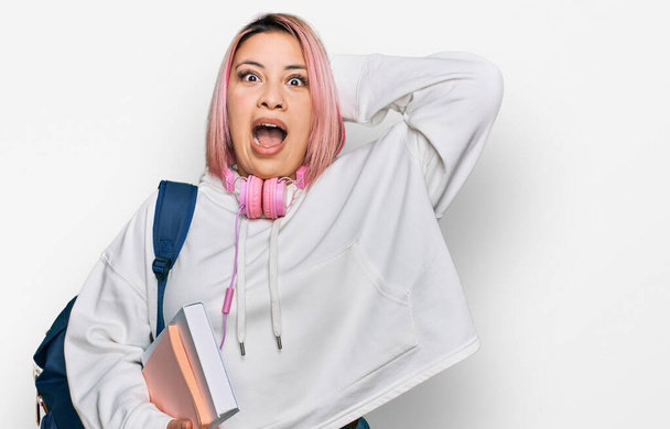 Іспанка з рожевим волоссям у студентському рюкзаку і навушниках божевільна і налякана руками на голову, налякана і здивована від шоку відкритим ротом.  - Фото, зображення