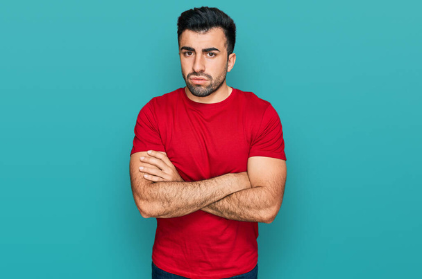 Hispanischer Mann mit Bart, lässig rotes T-Shirt, nervös, ablehnender Gesichtsausdruck mit verschränkten Armen. negative person.  - Foto, Bild
