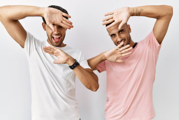 Young gay couple standing over isolated background smiling cheerful playing peek a boo with hands showing face. surprised and exited  - Photo, Image