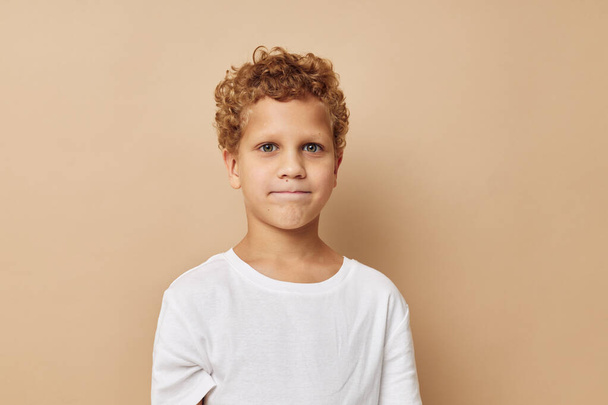 Cheerful boy with curly hair in a white t-shirt beige background - Valokuva, kuva