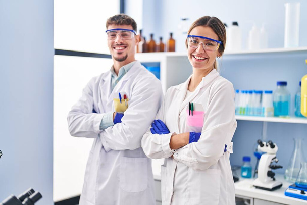 Jeune homme et jeune femme scientifiques travailleurs debout les bras croisés geste au laboratoire - Photo, image