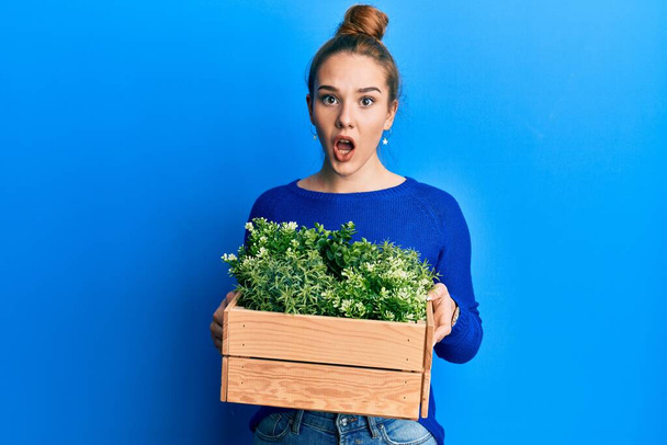 Young blonde woman holding wooden plant pot afraid and shocked with surprise and amazed expression, fear and excited face.  - Photo, Image