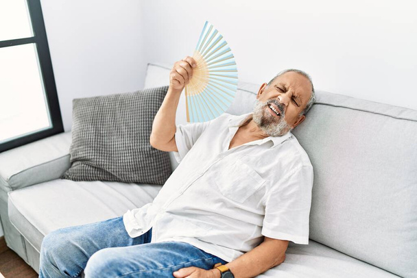 Senior uomo dai capelli grigi utilizzando ventilatore a mano a casa - Foto, immagini
