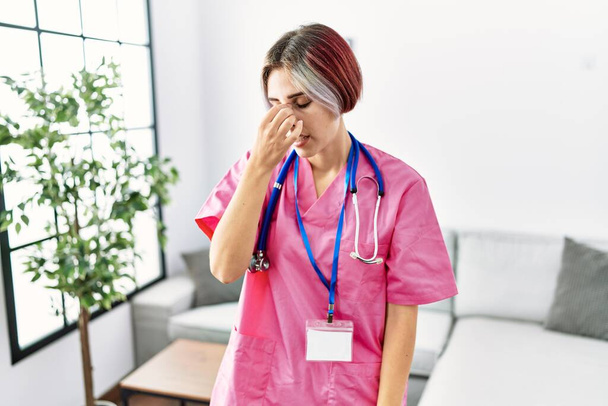 Young beautiful woman wearing doctor uniform and stethoscope tired rubbing nose and eyes feeling fatigue and headache. stress and frustration concept.  - Foto, Imagem