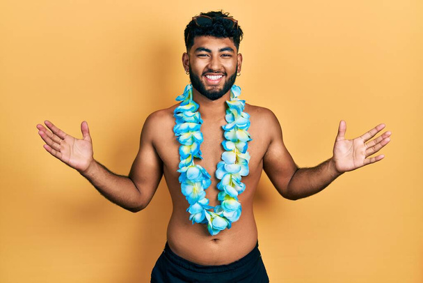 Arabische man met baard in badpak en Hawaïaanse lei viert overwinning met vrolijke glimlach en winnaarsuitdrukking met opgeheven handen  - Foto, afbeelding