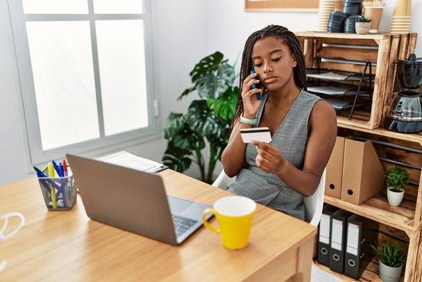 Молода афроамериканська бізнес-працівниця говорить на смартфоні, використовуючи кредитну картку в офісі. - Фото, зображення