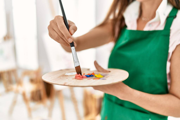 Orta yaşlı İspanyol kadın sanat stüdyosunda palet üzerine renk karıştırıyor. - Fotoğraf, Görsel
